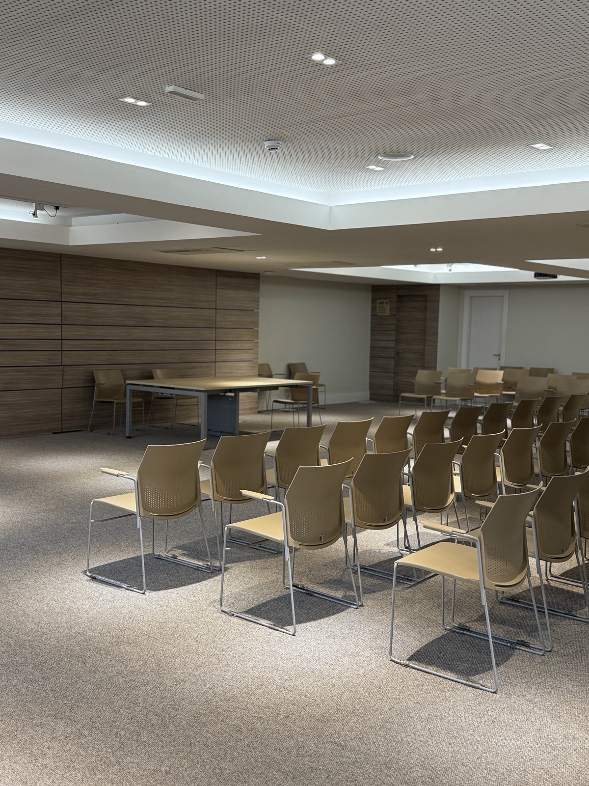 Mesa para palestrantes diante das cadeiras e do painel de madeira